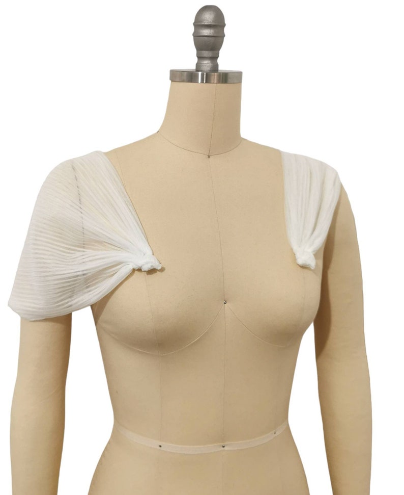 May include: White sheer fabric shoulder wraps with a pleated design. The wraps are tied at the shoulders with a knot.