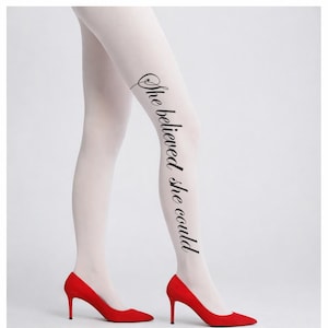 May include: White tights with the text "She believed she could" in black script. The tights are paired with red high-heeled shoes. The image is set against a plain white background.