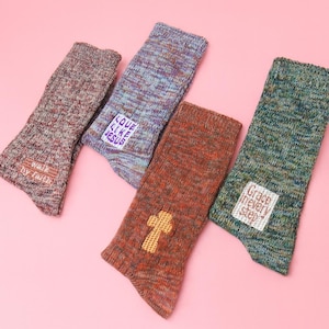 May include: Four pairs of colorful knit socks with religious-themed patches and designs. One pair has a cross, another says "Love Like Jesus," a third says "Grace in every step," and the last says "Walk by faith."