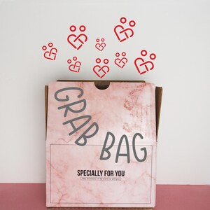 May include: A pink and brown cardboard box with the words "GRAB BAG" printed on the front. The box is open and there are red heart-shaped symbols with people inside floating above it. The text "SPECIALLY FOR YOU" is printed below the box.