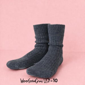 K&ouml;nnte beinhalten: Ein Paar anthrazitfarbene, gerippte Stricksocken. Die Socken sind oben umgeschlagen und werden auf rosa Hintergrund pr&auml;sentiert. Der Text "WoolSolidGray US7-10" befindet sich unten.