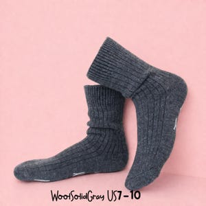 K&ouml;nnte beinhalten: Ein Paar dunkelgraue Rippstrick-Socken mit dem Text "WoolSolidGray US7-10" unten. Die Socken werden vor einem rosa Hintergrund pr&auml;sentiert. Die Socken haben einen umgeschlagenen Bund und wei&szlig;e Akzente an den Zehen.