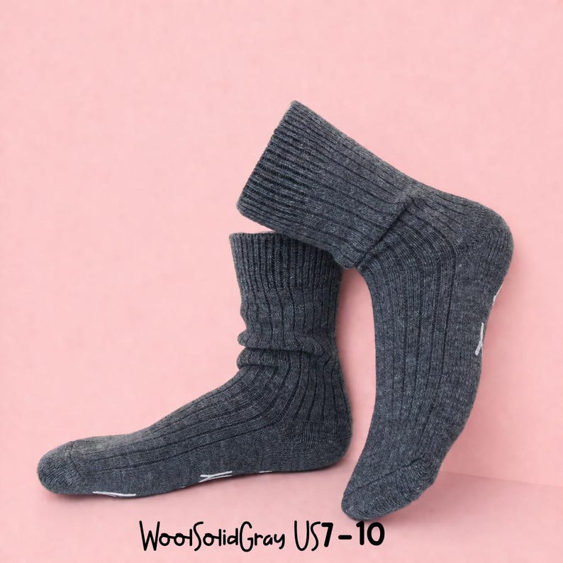 K&ouml;nnte beinhalten: Ein Paar dunkelgraue Rippstrick-Socken mit dem Text "WoolSolidGray US7-10" unten. Die Socken werden vor einem rosa Hintergrund pr&auml;sentiert. Die Socken haben einen umgeschlagenen Bund und wei&szlig;e Akzente an den Zehen.