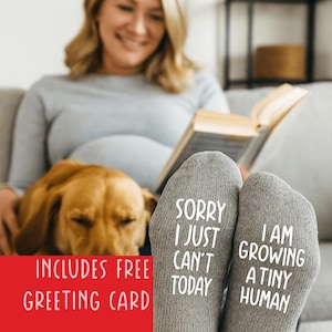 Puede incluir: Un par de calcetines de punto gris con texto blanco en las suelas. El calcet&iacute;n izquierdo dice SORRY I JUST CAN'T TODAY y el derecho dice I AM GROWING A TINY HUMAN. Los calcetines est&aacute;n confeccionados con un tejido suave y texturizado.