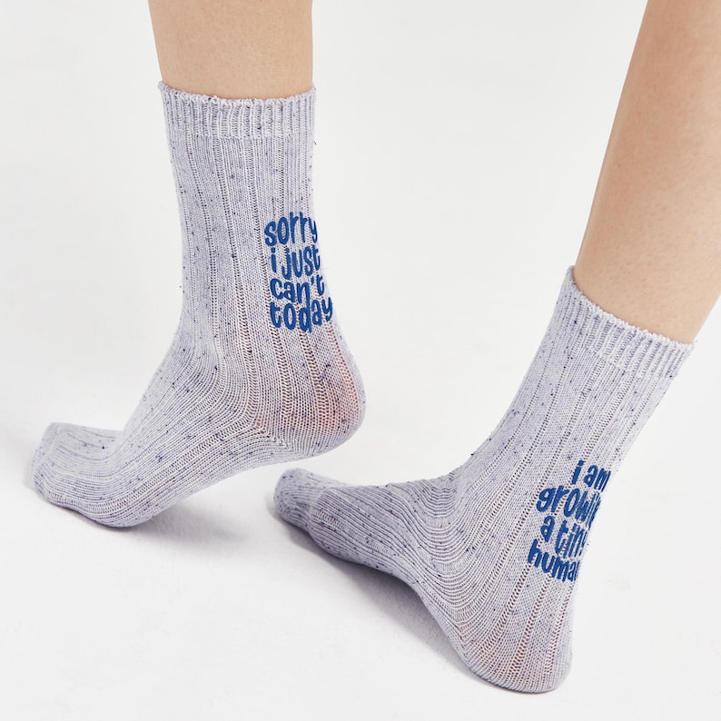 socks with a humorous message about pregnancy, emphasizing the importance of self-care while growing a tiny human. Model wearing speckled blue ribbed socks with matching “Sorry I just can’t today” and “I am growing a tiny human” embroidery. Comfortable cotton maternity socks by Sockmate.