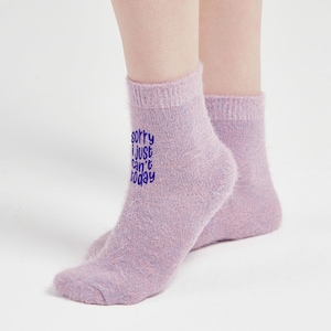 Model wearing fluffy lilac fuzzy socks with purple “Sorry I just can’t today” embroidery, photographed on white floor. Soft and warm cozy socks for relaxing days.
