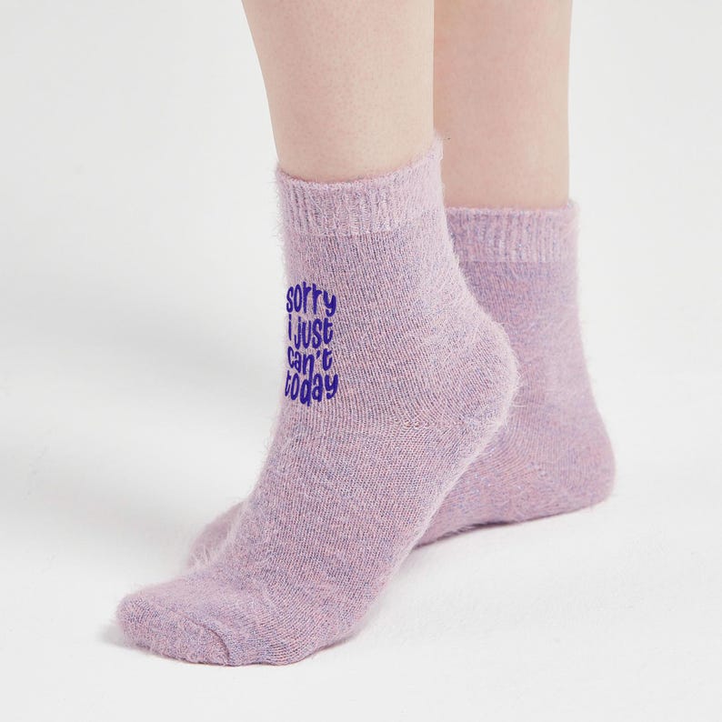 Model wearing fluffy lilac fuzzy socks with purple “Sorry I just can’t today” embroidery, photographed on white floor. Soft and warm cozy socks for relaxing days.