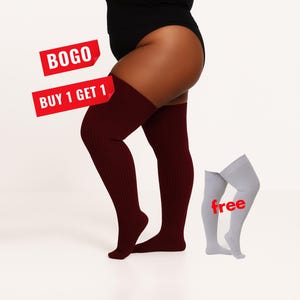 Puede incluir: Un par de calcetines altos de canalé color granate oscuro usados en las piernas, acompañados por un par separado de calcetines altos de canalé color gris claro. La imagen incluye textos superpuestos en rojo que dicen BOGO, BUY 1 GET 1 y free.