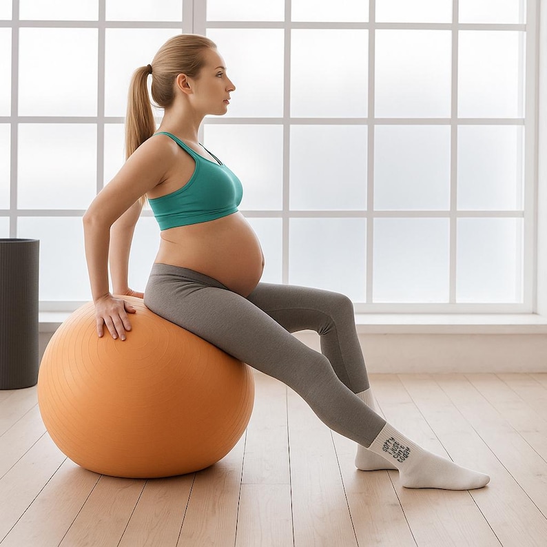 Pregnant woman sitting on orange yoga ball in a bright studio wearing white pregnancy socks with motivational text. Comfortable prenatal socks ideal for pilates or yoga.