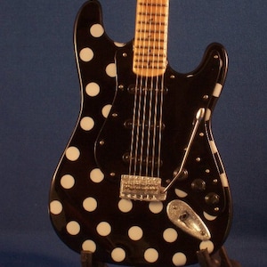 May include: A black electric guitar with white polka dots. The guitar has a wooden fretboard and a chrome bridge.