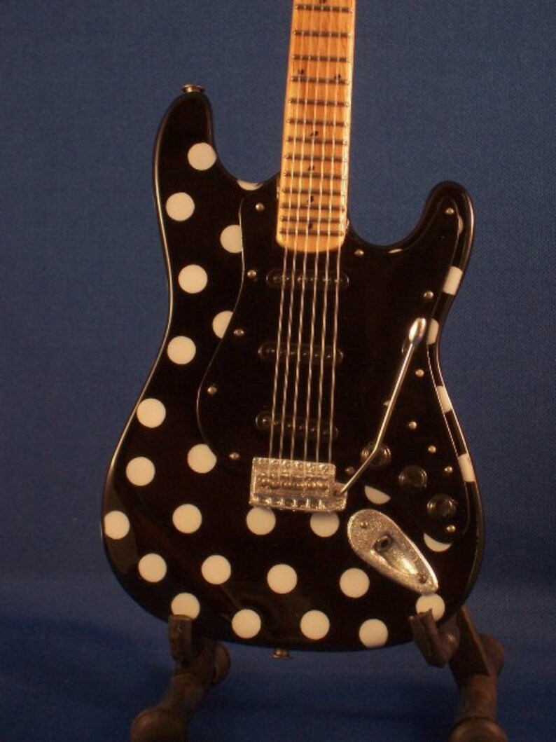 May include: A black electric guitar with white polka dots. The guitar has a wooden fretboard and a chrome bridge.