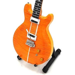 May include: A bright orange electric guitar with a black pickguard and a white stripe down the center. The guitar is on a black stand.