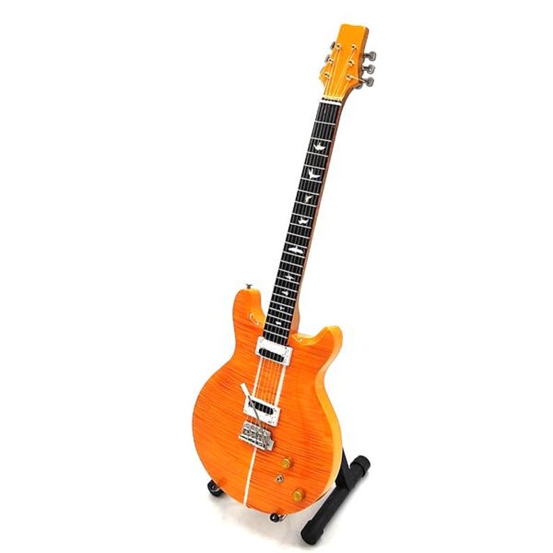 May include: A vintage-style electric guitar with a natural wood finish and a black pickguard. The guitar has a single cutaway body and a set of six tuning keys at the headstock.