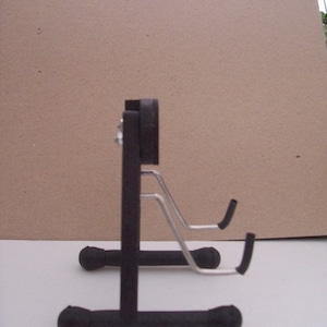 May include: A black metal guitar stand with two adjustable arms. The stand has a round base and a rectangular support.