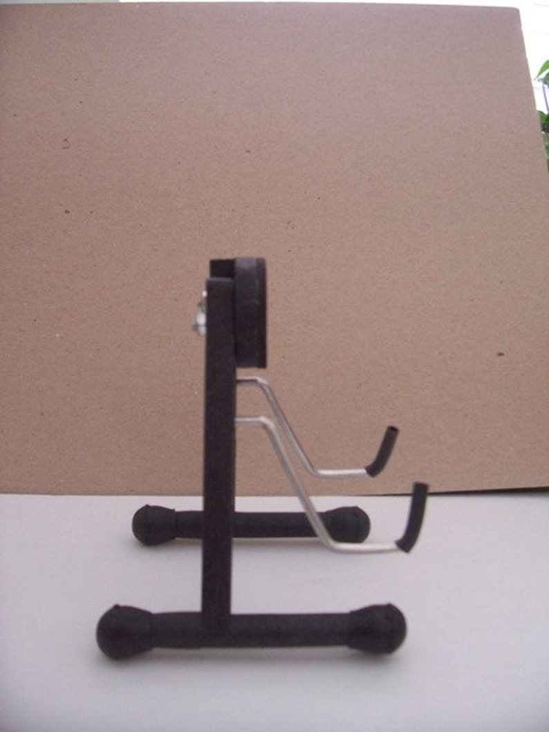 May include: A black metal guitar stand with two adjustable arms. The stand has a round base and a rectangular support.