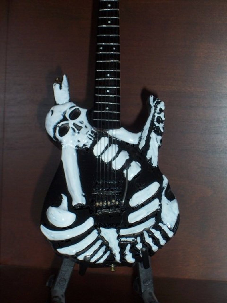 May include: A black electric guitar with a white skeleton design. The guitar has a black body and a black neck with white fret markers. The skeleton design is painted on the body of the guitar.