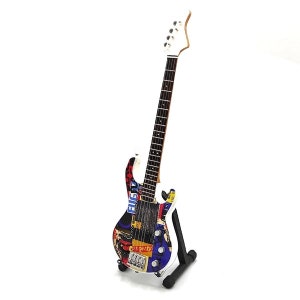 May include: A white electric bass guitar with a multi-colored design featuring various band names and logos, including "Elvis", "Sex Pistols", and "The Clash". The guitar is on a black stand.