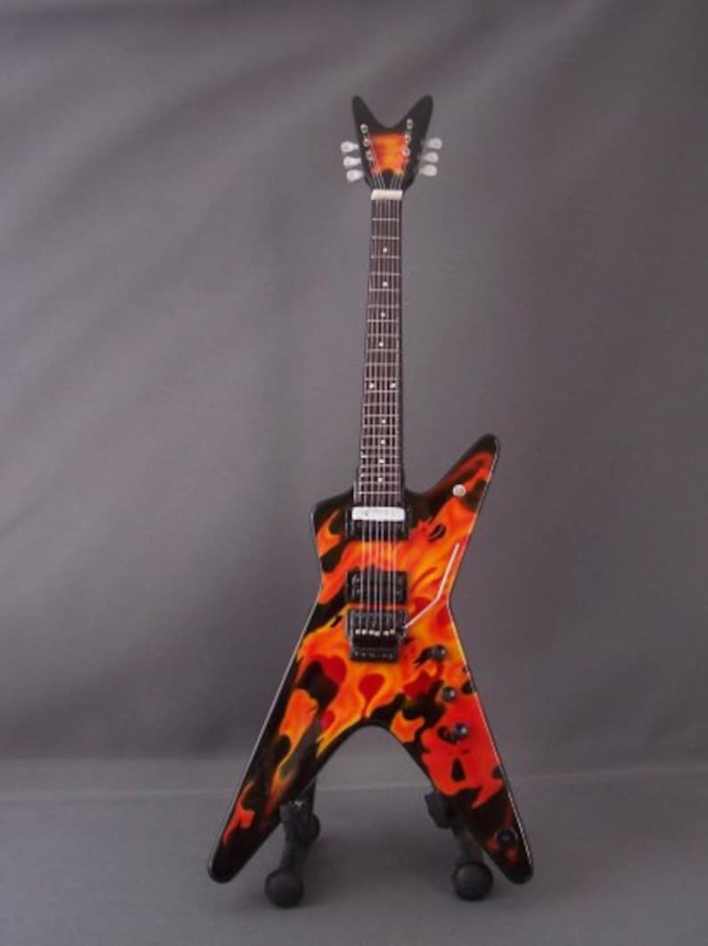 Puede incluir: Una guitarra el&eacute;ctrica negra con un dise&ntilde;o de llamas en naranja y rojo. La guitarra tiene una pala puntiaguda y un cuerpo en forma de V voladora.