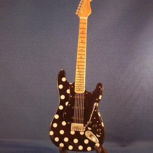 May include: A black electric guitar with white polka dots, on a black stand. The guitar has a maple neck and a rosewood fretboard.