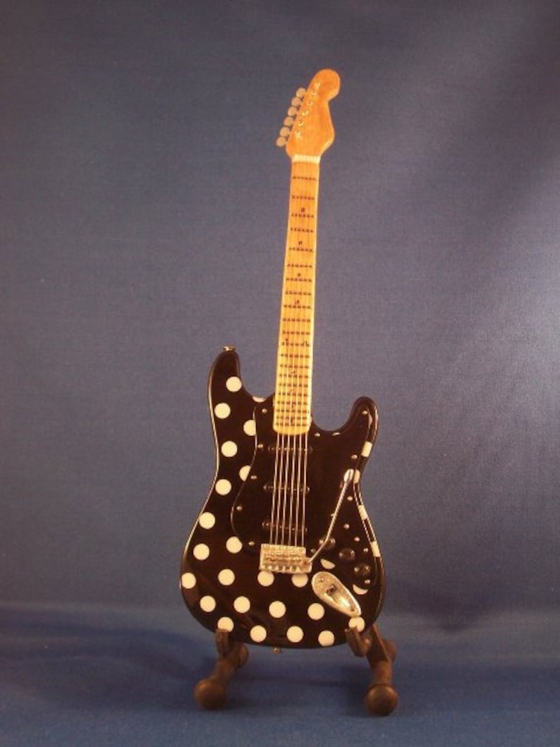 May include: A black electric guitar with white polka dots, on a black stand. The guitar has a maple neck and a rosewood fretboard.