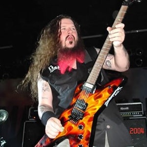 Puede incluir: Un hombre con el pelo largo y rojo rayado toca una guitarra el&eacute;ctrica negra y naranja con llamas pintadas en el cuerpo. La guitarra tiene una golpeador negro y una clavija de afinaci&oacute;n plateada.