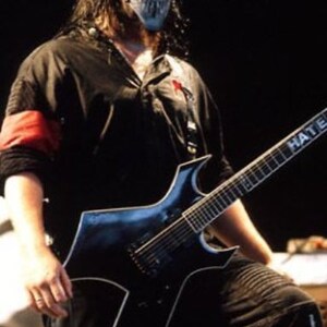 May include: A man wearing a black and white skull mask plays a black electric guitar with the word "Hate Eternal" written on the neck.