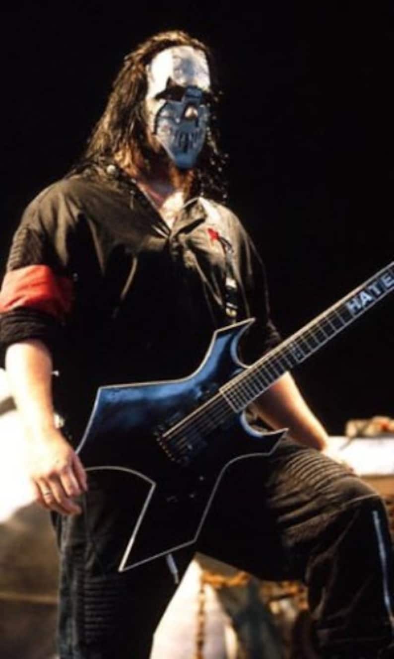 May include: A man wearing a black and white skull mask plays a black electric guitar with the word "Hate Eternal" written on the neck.