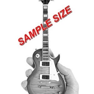 Puede incluir: Una guitarra el&eacute;ctrica en miniatura con un acabado marr&oacute;n y negro. La guitarra tiene un cuerpo de una sola forma y una pala negra con clavijas cromadas. La guitarra est&aacute; siendo sostenida en una mano.