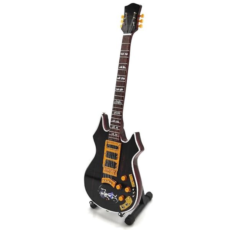 Puede incluir: Una guitarra el&eacute;ctrica negra con detalles dorados y una forma de cuerpo &uacute;nica. La guitarra tiene un diapas&oacute;n detallado y se muestra en un soporte negro. El cuerpo presenta un dise&ntilde;o gr&aacute;fico colorido.