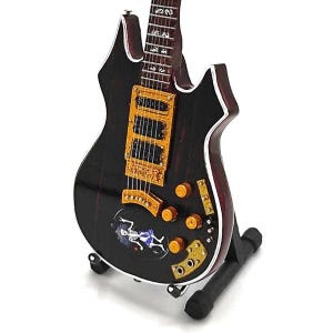 Puede incluir: Miniatura de guitarra el&eacute;ctrica negra con herrajes dorados y un gr&aacute;fico de esqueleto en el cuerpo. La guitarra se exhibe en un soporte negro. La guitarra tiene un acabado de madera oscura con ribetes blancos.