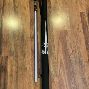 May include: A white lightsaber with a black handle and a black carrying case with a white logo. The case has a shoulder strap.