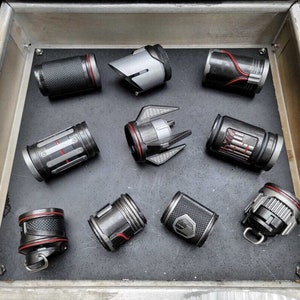 May include: A collection of nine small, cylindrical objects with a metallic gray finish and red accents. The objects have various designs and textures, including a textured surface, a ribbed surface, and a smooth surface. Some of the objects have a small, red ring around the top.