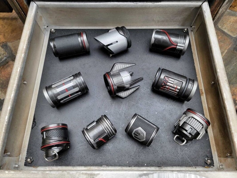 May include: A collection of nine small, cylindrical objects with a metallic gray finish and red accents. The objects have various designs and textures, including a textured surface, a ribbed surface, and a smooth surface. Some of the objects have a small, red ring around the top.