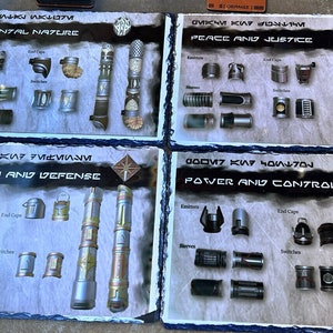 May include: Four slate tiles with different lightsaber parts and designs. Each tile has a title in a fictional language and an English translation. The titles are "Elemental Nature", "Peace and Justice", "Protection and Defense", and "Power and Control".