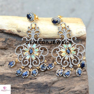 May include: A pair of gold and silver dangle earrings with a floral design. The earrings feature white opals and blue sapphires.
