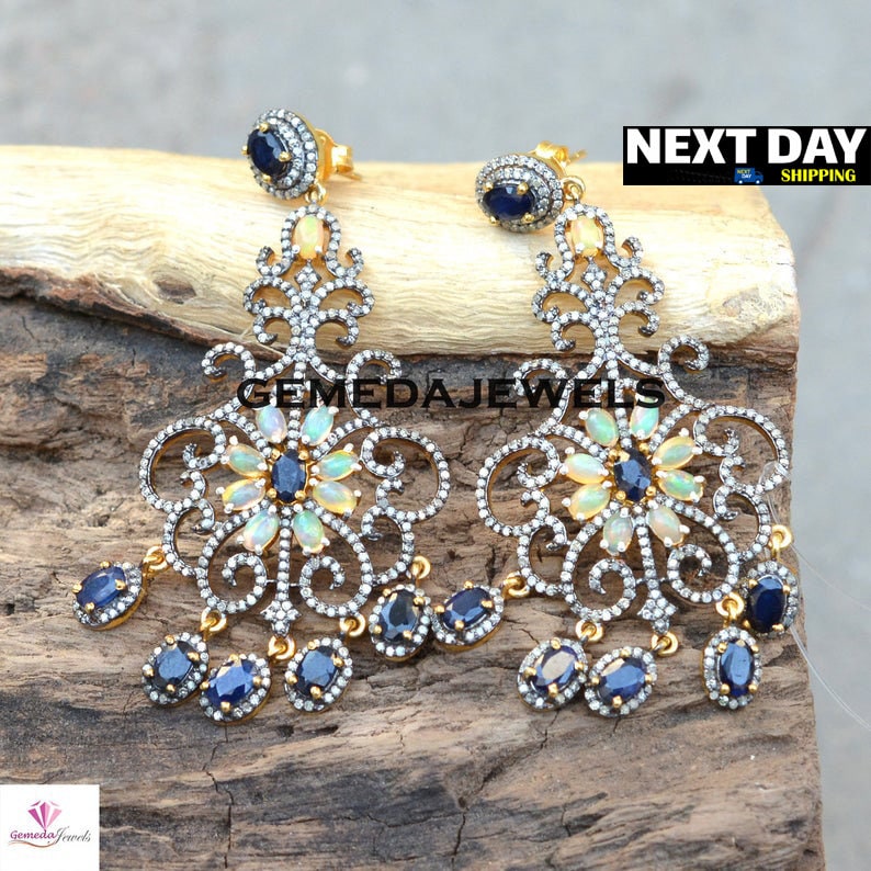 May include: A pair of silver filigree earrings with dangling blue and white gemstones. The earrings feature a floral design with a central opal and smaller blue gemstones.