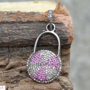 May include: A silver pendant with a round, pave-set design featuring pink and white stones. The pendant is attached to a silver bail.