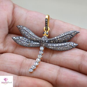 Peut inclure: Un pendentif en argent en forme de libellule avec une cha&icirc;ne en or et des diamants noirs. Les ailes de la libellule sont d&eacute;ploy&eacute;es et la cha&icirc;ne est attach&eacute;e au sommet de la t&ecirc;te de la libellule.