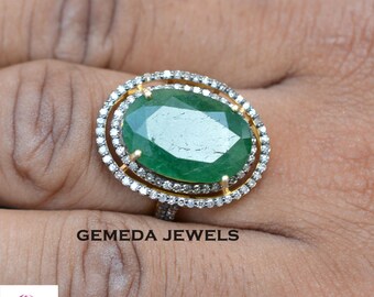 May include: A gold ring featuring a large oval emerald gemstone encircled by two rows of smaller diamonds. The ring is worn on a finger.