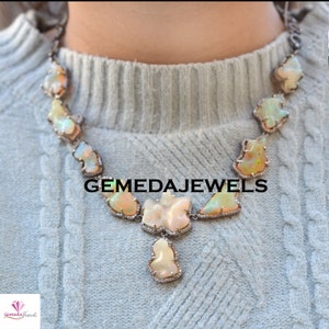 May include: A silver necklace with a pendant featuring a large, white opal stone surrounded by smaller diamonds. The necklace is made up of a series of smaller opal stones, each surrounded by diamonds. The necklace is called "GEMEDAJEWELS".