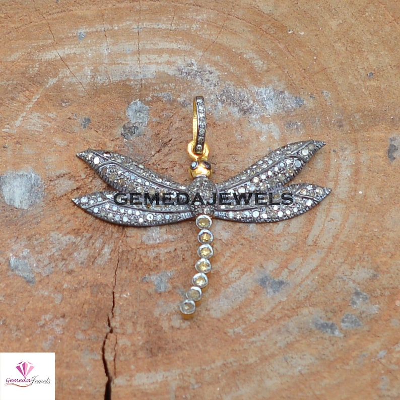 Peut inclure: Un pendentif en argent en forme de libellule serti de diamants clairs et jaunes. Les ailes de la libellule sont orn&eacute;es de diamants sertis pav&eacute;. Le pendentif est pr&eacute;sent&eacute; sur une surface en bois.