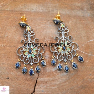 May include: A pair of silver and gold dangle earrings with a floral design. The earrings feature blue and white gemstones.