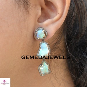 May include: Silver dangle earrings with three opal stones set in a silver frame with small diamonds. The earrings are a light blue color and have a unique, irregular shape.