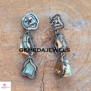 May include: A pair of silver dangle earrings with a white opal stone set in a silver frame. The earrings have a geometric design and are accented with small diamonds.