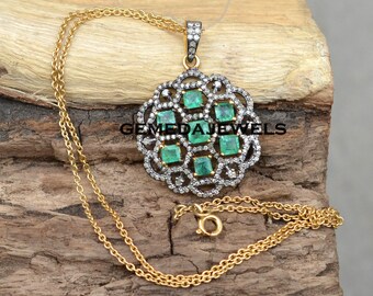 May include: A gold chain necklace with a pendant featuring a circular design with nine square emerald green gemstones surrounded by smaller diamonds. The pendant is attached to a gold chain with a lobster clasp. The text "GEMEDAJEWELS" is visible on the pendant.