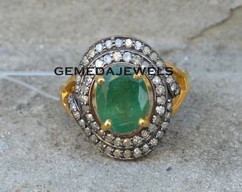 May include: A gold ring featuring a large oval emerald gemstone, encircled by a double halo of small diamonds. The diamonds are set in silver.