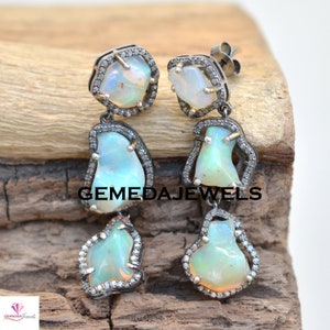 May include: A pair of silver dangle earrings with three opal stones and diamond accents. The earrings are set in a silver setting and have a delicate design.
