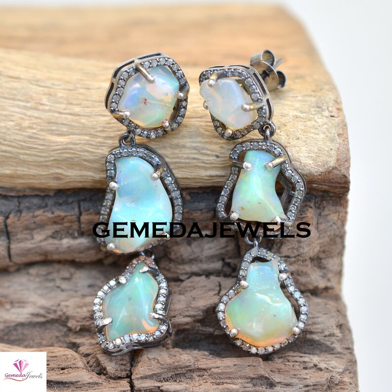 May include: A pair of silver dangle earrings with three opal stones and diamond accents. The earrings are set in a silver setting and have a delicate design.