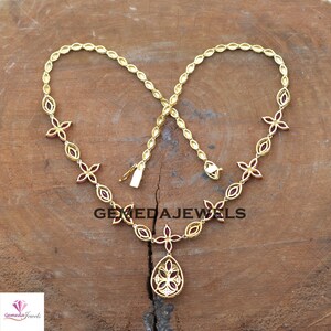 May include: A gold necklace with a teardrop pendant featuring a red flower design. The necklace is adorned with red flower accents and oval-shaped stones.