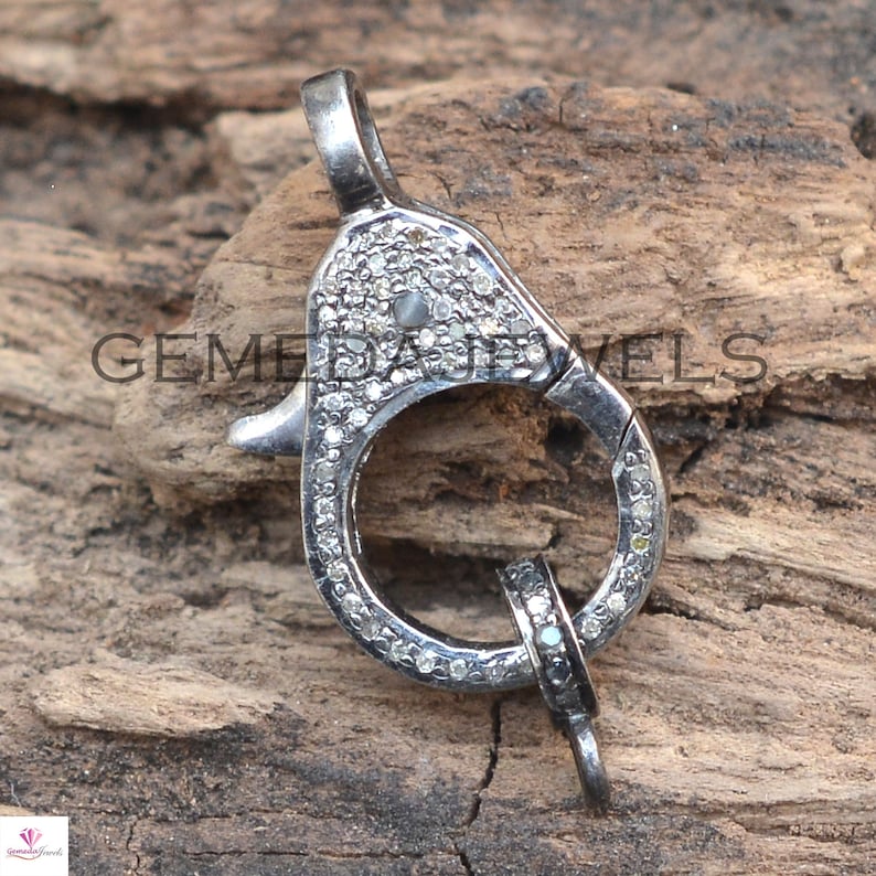 May include: Silver tone clasp with a round ring and a small hook. The clasp is covered in small, clear diamonds.